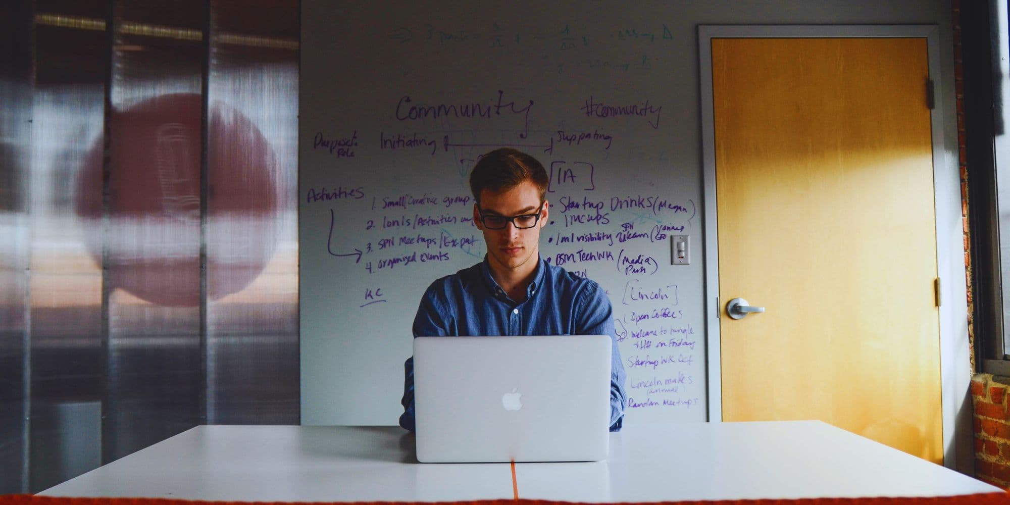 A person working on a laptop in front of a whiteboard with startup and VC notes.